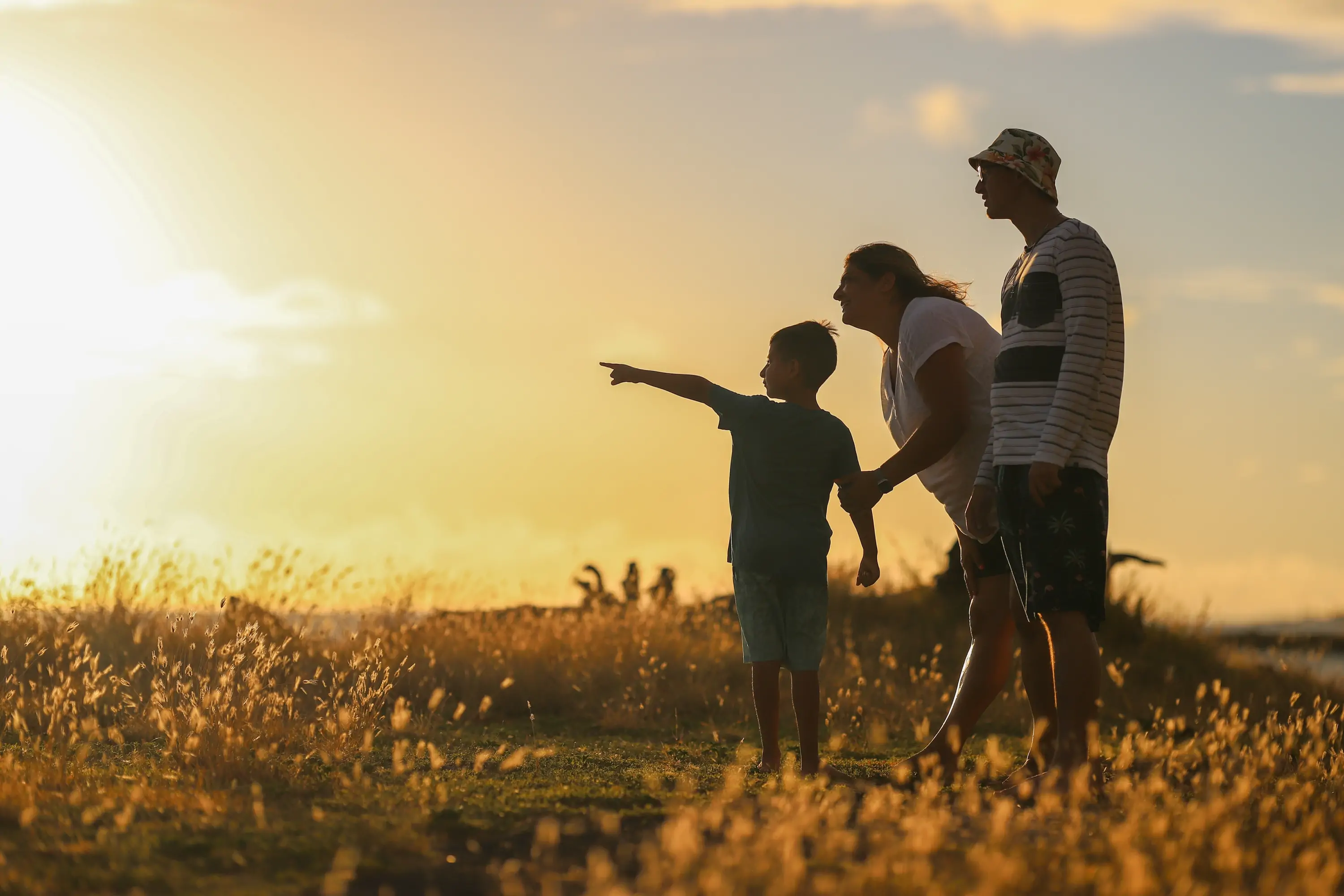 Caucasian mother and father with son in field. Son is pointing out into the field, as his parents watch, by his side.